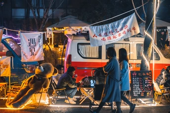 一些人坐在食品卡车旁边的一排椅子上。