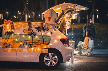 夜晚停在街道上的一辆小汽车旁 有人们和一只狗在下面 在遮阳伞下。