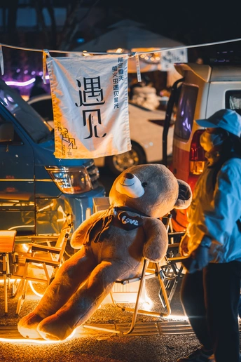 一位妇女站在一只坐在椅子上的泰迪熊旁边 夜晚的街道上。