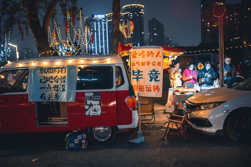 夜幕下 一辆红色和白色的小货车停在红色和白色的小餐车旁边。