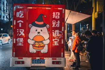 夜晚停在人行道上的红色卡车 上面有一个汉堡 人们站在人行道上。