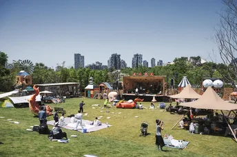 远处有一个草地上有很多人在毯子和帐篷上 背景中有一个城市。