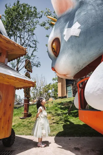 一个小女孩站在一个人旁边 正在看一个充气动物。