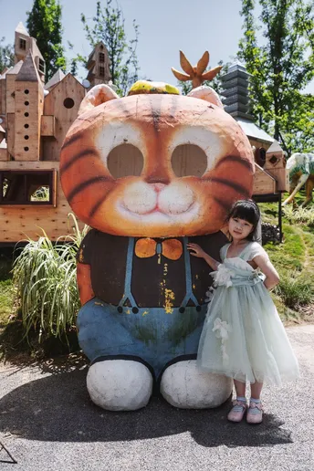 一个小女孩穿着裙子站在一只大型毛绒玩具旁边