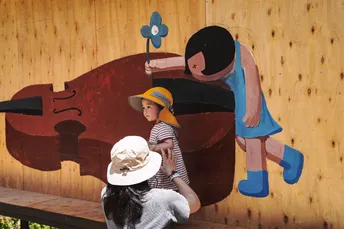 墙上的一名女子抱着一把小提琴的一名男孩坐在长凳上 狗站立着 墙上的一名女子坐在墙上。