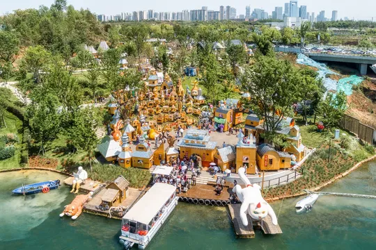 河中央有一个岛屿 岛上有人在玩 背景是一个城市 上方是一个游乐场的鸟瞰图。