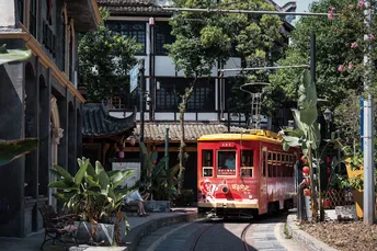 一辆红色和黄色的有轨电车或手推车在城市街道上行驶 两侧有建筑和树木。