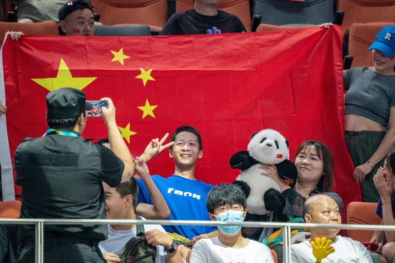 许多人正在拍照 其中一个人戴着口罩 手里拿着中国国旗。