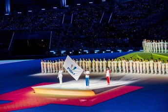 表演者站在体育场舞台上 在奥林匹克团队旗帜的开幕式期间。