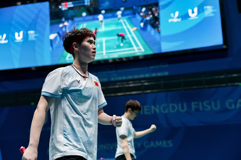 一个年轻人手里拿着网球拍 站在一个有网球运动员在上面打球的屏幕前面。