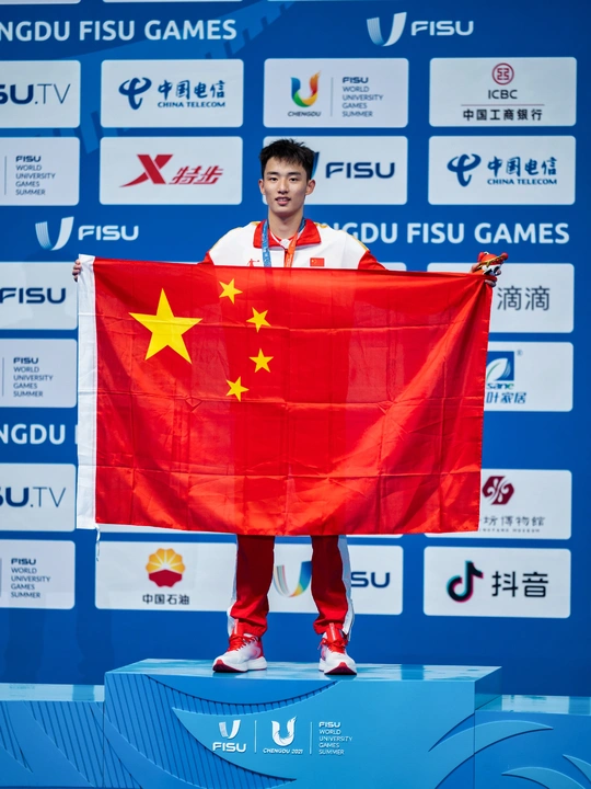 一位举着红旗的男子站在领奖台上 手里拿着一枚金牌。