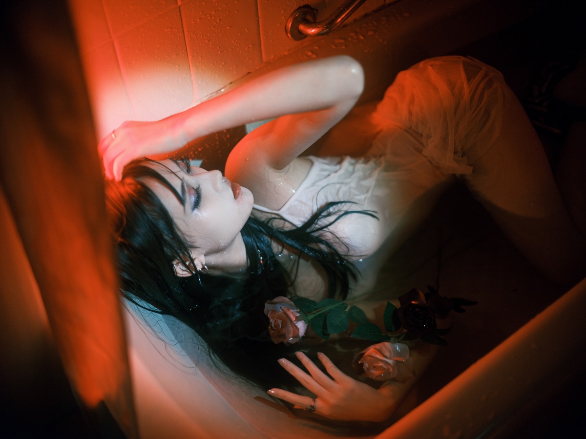 一个年轻女子躺在浴缸里 浴缸里充满了暗房间的红色光线。