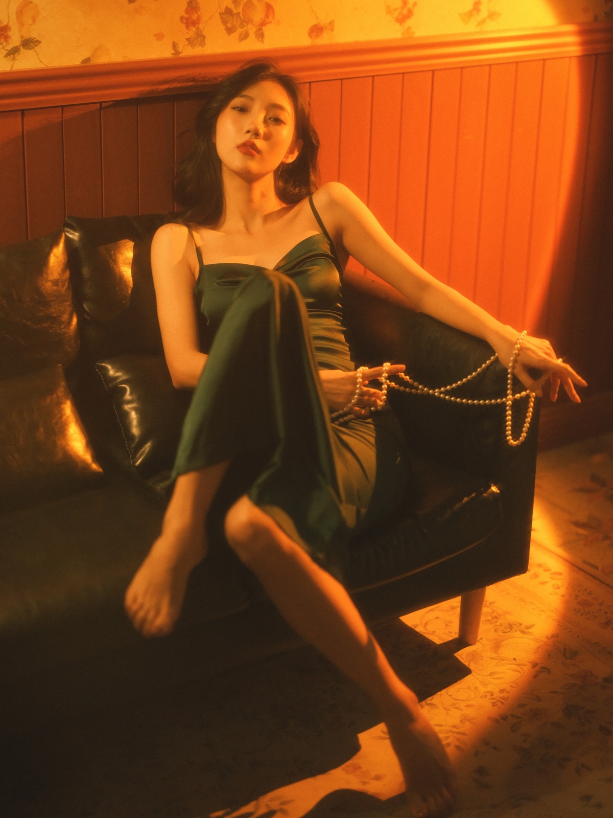 一个穿着绿色连衣裙的年轻女子坐在沙发上 双腿交叉 在一个光线昏暗的房间里。