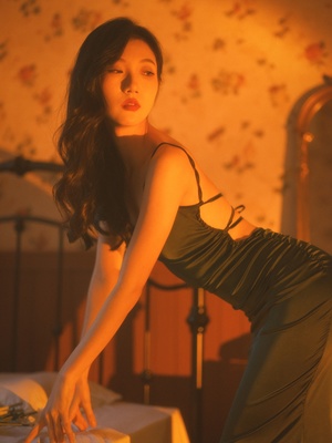 一个穿着黑色连衣裙的年轻女子在一个卧室里摆姿势 床在旁边。