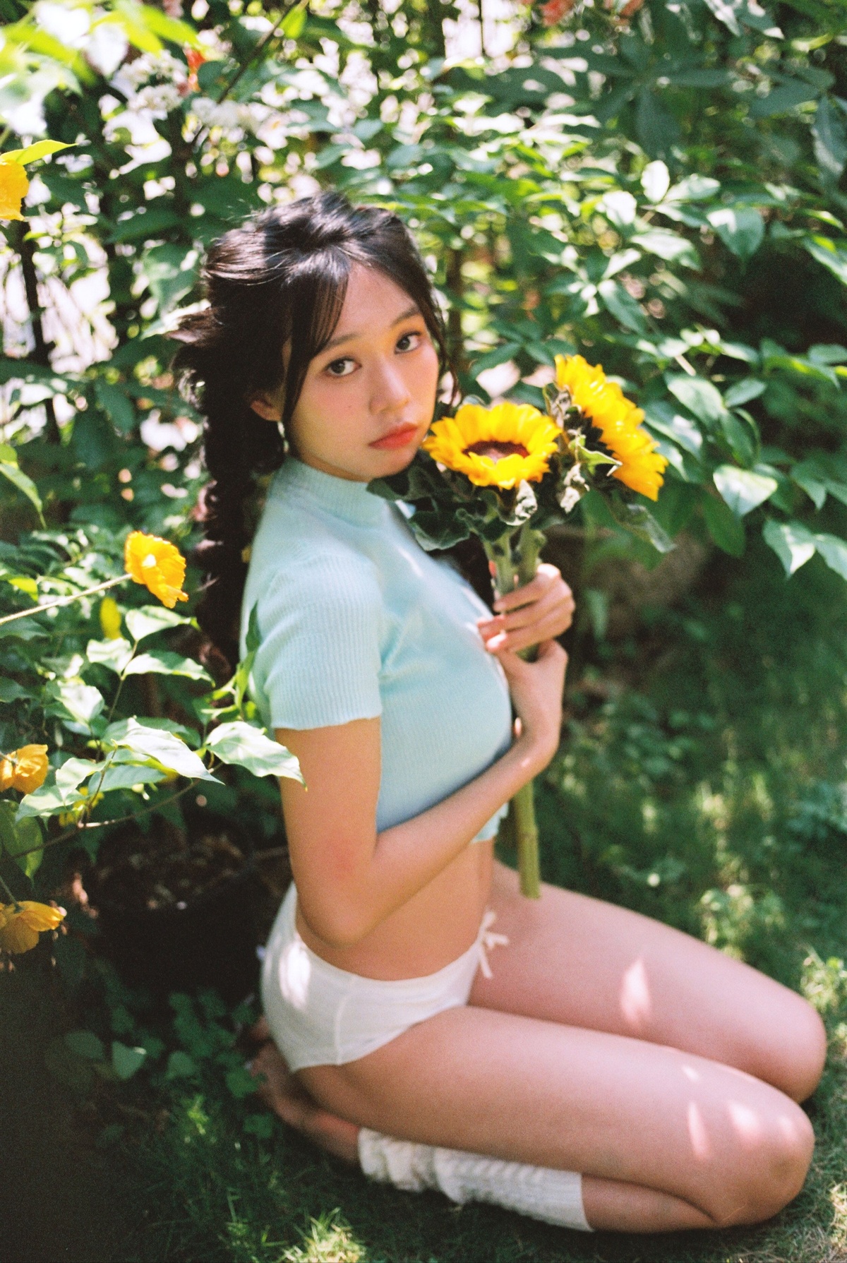 一位穿着蓝色衣服的年轻女子抱着黄色花坐在花园里