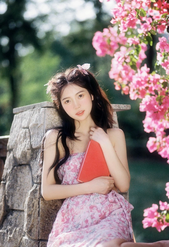 一个穿着连衣裙的年轻女子抱着红色书籍坐在长凳上