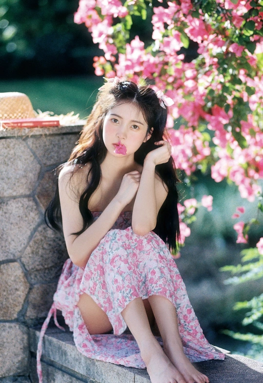 一位穿着连衣裙的美丽年轻女子坐在粉色花朵前