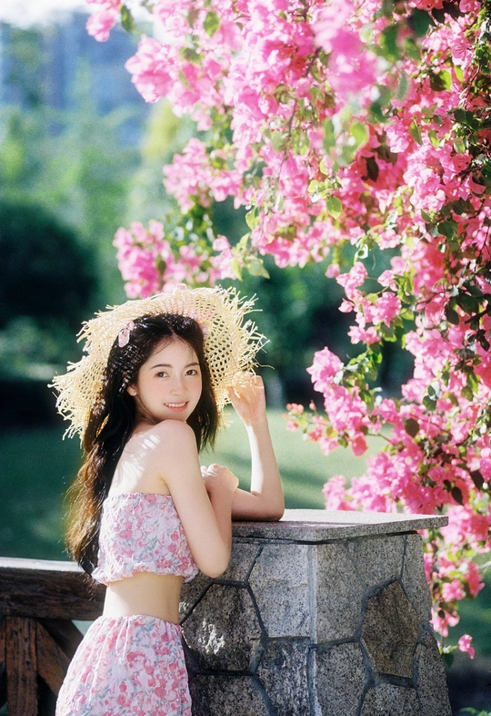 一位穿着连衣裙和草编帽子的年轻女子站在粉色花朵前
