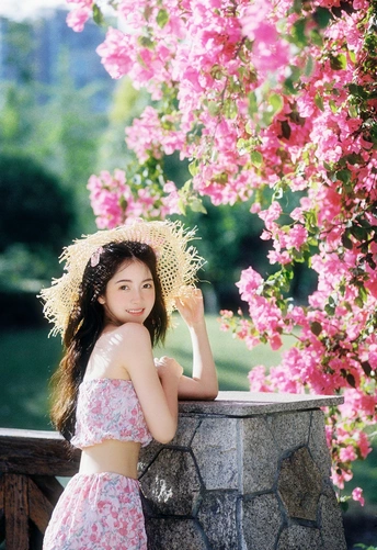 一位穿着连衣裙和草编帽子的年轻女子站在粉色花朵前