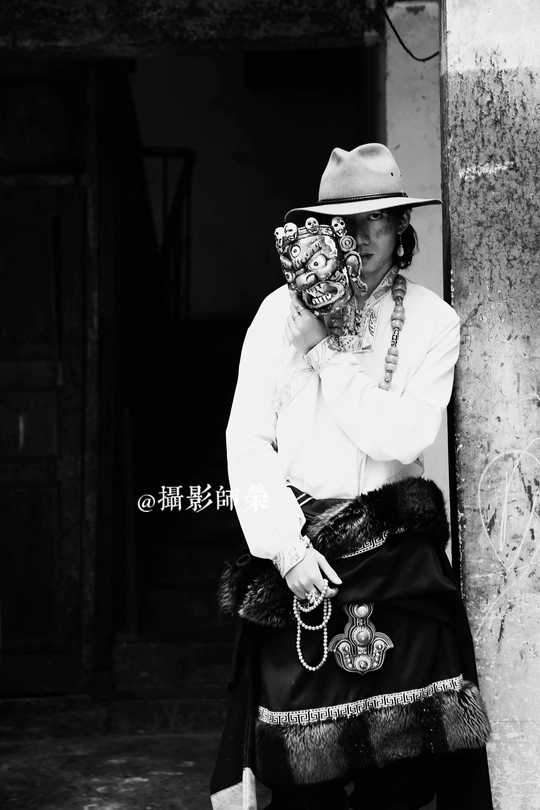 一位脸上戴着传统口罩的老妇人靠着一根柱子坐在一栋楼前