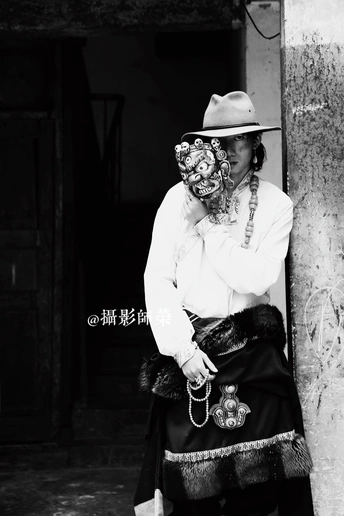 一位脸上戴着传统口罩的老妇人靠着一根柱子坐在一栋楼前