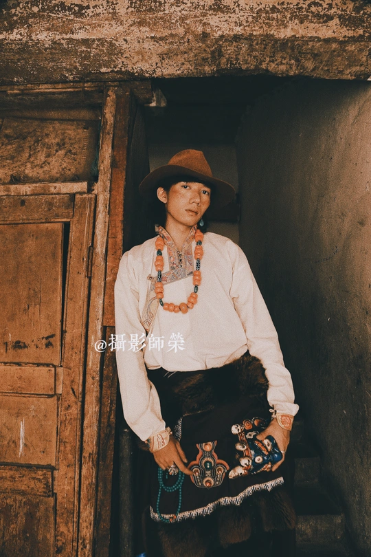 一个穿着传统服装、戴着帽子的女人站在一所老房子门口的画像