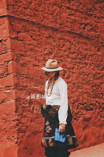 一位戴着牛仔帽、拿着包的老妇人走过一堵红砖墙