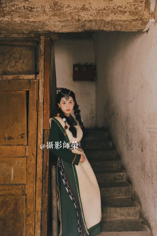 一位穿着传统服装的年轻女子站在一栋老建筑物的台阶上 穿着一件绿色的裙子。