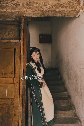 一位穿着传统服装的年轻女子站在一栋老建筑物的台阶上 穿着一件绿色的裙子。