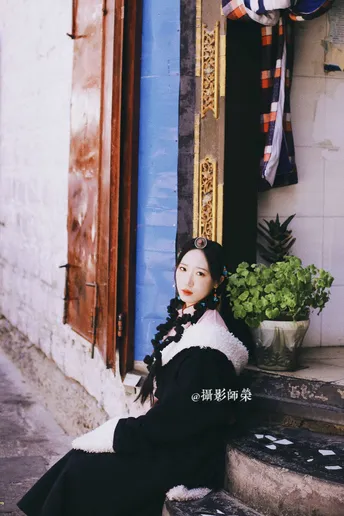 一位穿着传统服装的年轻女子坐在街道上一栋建筑物的台阶上。