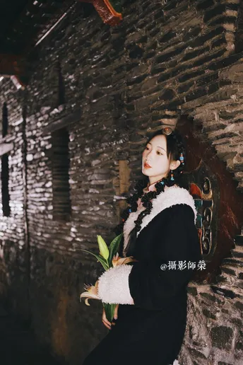 一位穿着传统服装的女士拿着花站在一条小巷子里