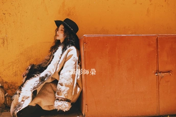 一个戴黑色帽子和大衣的女人坐在橙色墙壁上