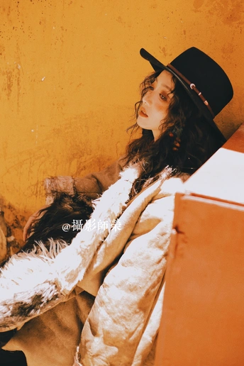 一位穿着皮草大衣和黑色帽子 坐在墙边的女士