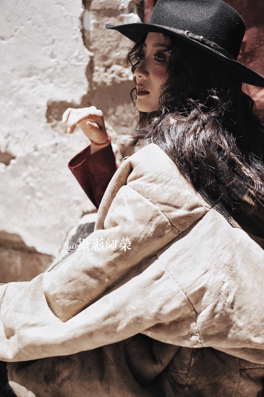 一位戴黑色帽子、白色外套的女人站在一面墙前