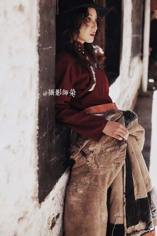 一位戴黑色帽子倚靠在墙边的年轻女子