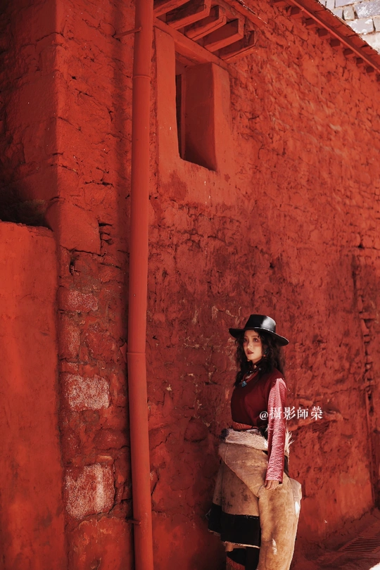 一位戴帽子的年轻女子站在一幅红色的墙前