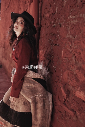 一个戴黑色帽子坐在骆驼上 靠在红色砖墙上的年轻女子