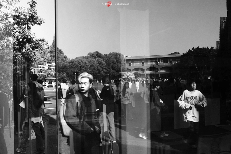 一张黑白照片 人们走在一条街道上 一个男人站在窗户里。