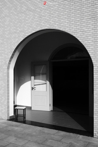 一张黑白照片 展示了一扇带有拱门和一张坐在门前长凳上的照片。