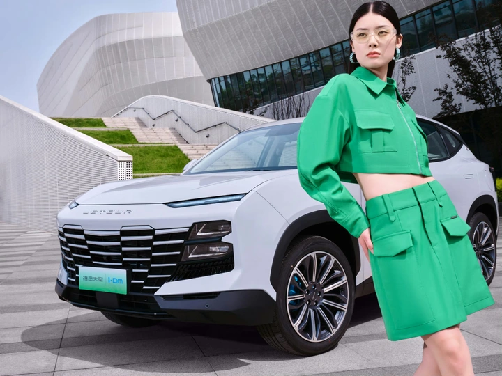 一位穿着绿色连衣裙和外套的女士走过街道上的一辆车