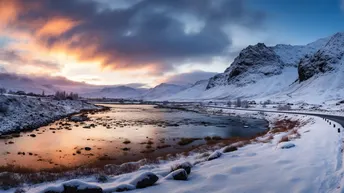 夕阳下山脉边的一条河上的雪景道路