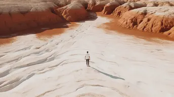 一个人站在峡谷中间 地面上有红色的沙子和水。