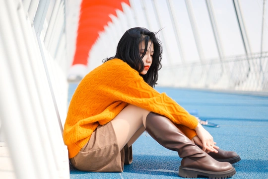 一个穿着橙色毛衣和蓝色靴子的女人坐在桥的地板上