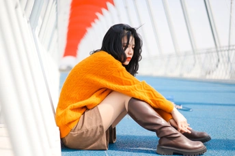 一个穿着橙色毛衣和蓝色靴子的女人坐在桥的地板上