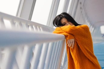 一位身穿橙色长袍的年轻女子站在靠着阳台栏杆的桥上
