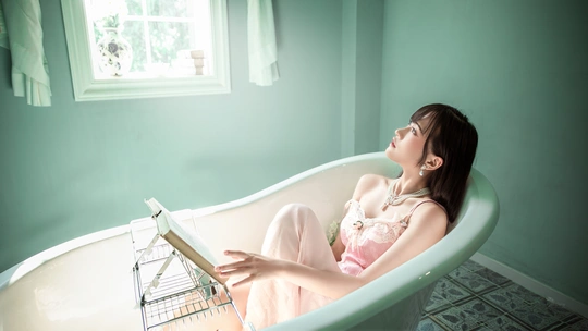 一个年轻女子坐在粉色浴缸里阅读 位于窗户边的浴室。