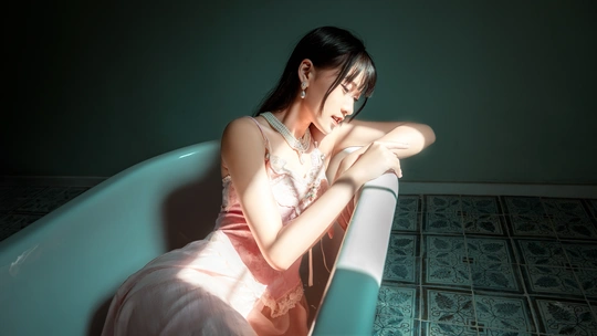 一个穿着连衣裙的年轻女子坐在蓝色的浴缸里 在一个铺有瓷砖的房间里。