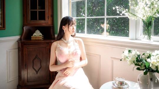 一个穿着粉红色连衣裙的年轻女子坐在一个带窗户和一束白色花的花瓶的房间里