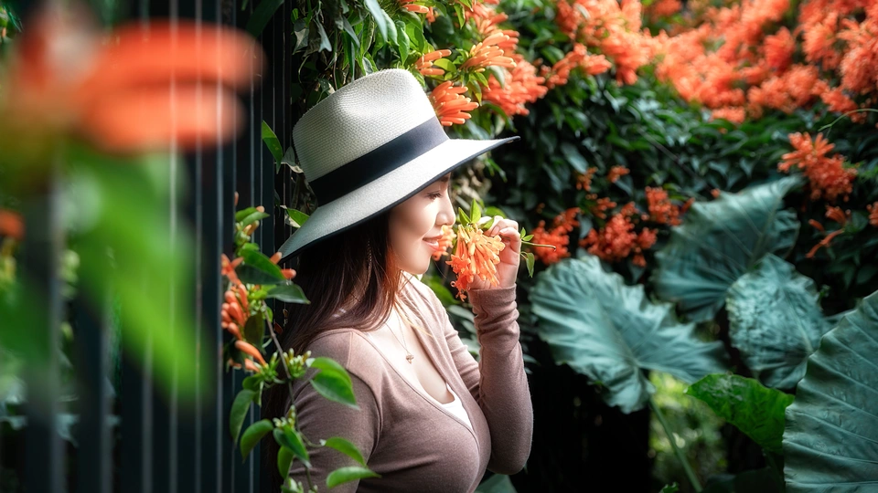 一位戴黑色礼帽和白色帽子的女士站在围栏前 围栏上开着橙色的花。