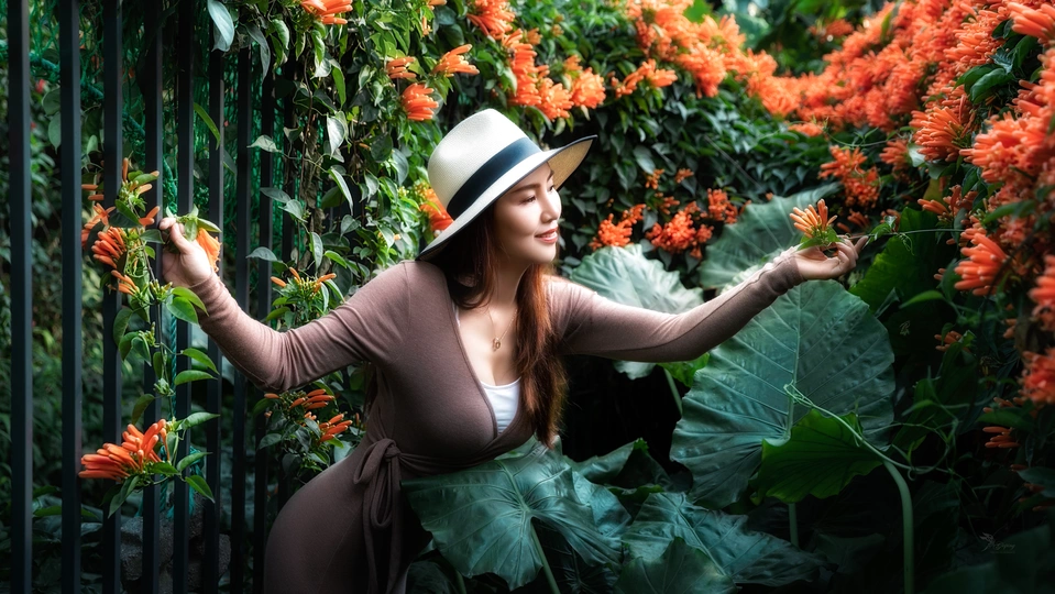 戴帽子的一位年轻女子站在一扇有橙色花朵的围墙前